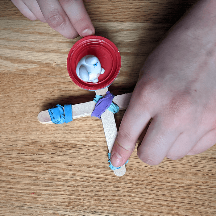 Photo of finished popsicle stick catapult with a small toy rabbit figurine in the basket and ready to launch