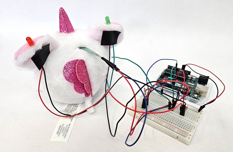 Rear view showing circuit components on stuffed animal and connected to breadboard with jumper wires