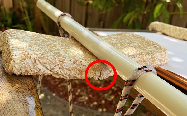 Closeup of a panel being tested.  The panel is bending, forming a wide V-shape. 
     A fracture is visible under the dowel, starting from the bottom of the panel. 