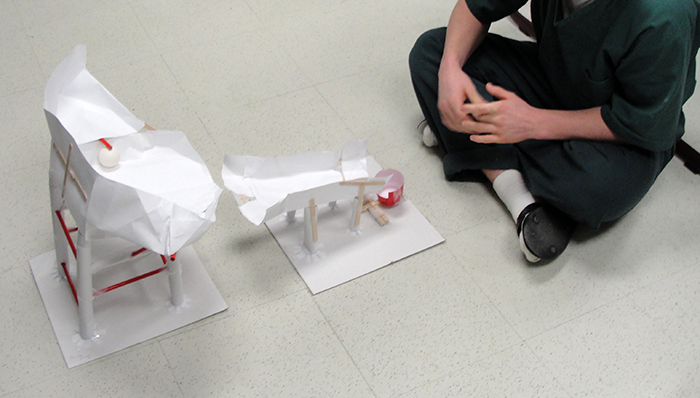 A student sitting next to a paper ball launcher and catcher