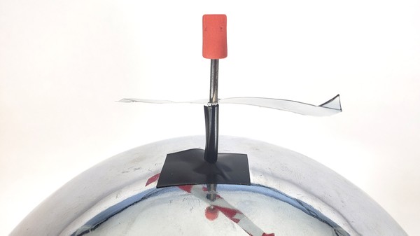 An aluminum propellor with pointed tips, mounted on a nail that is taped to top of Van de Graaff generator 