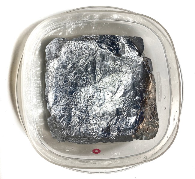 A plastic container, roughly 10 centimeters square, lined with a sheet of aluminum foil that has been crushed and then re-flattened. 