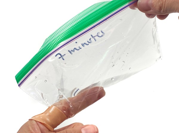 A hand holding a resealable plastic bag containing some water.