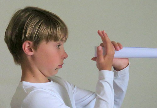 A child holds a hand and a paper tube near their face