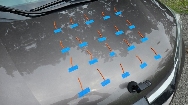Lengths of yarn, arranged in a 4 by 5 grid, taped to the hood of a car.