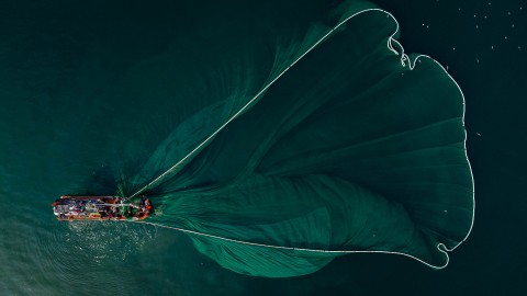 An aerial view of a fishing boat pulling a net through the ocean
