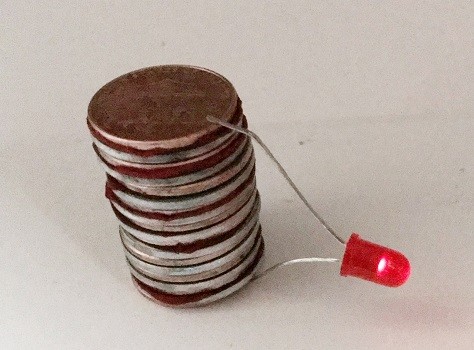 A stack of coins with a wire and light connecting the top and bottom coins