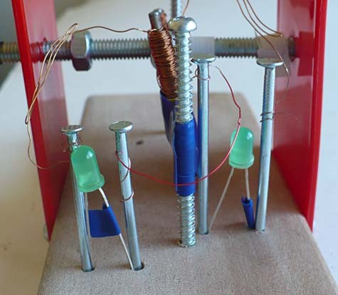 Two LEDs are connected in series using four nails and copper wire