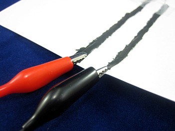 Alligator clips attached to two lines of conductive ink on a piece of paper
