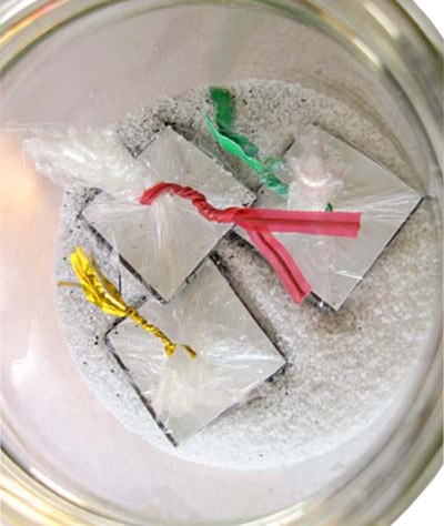Three squares of magnetic tape wrapped in plastic sit in a jar of salt and iron filings