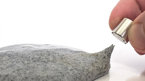 A blob of gray slime. Fingers hold a magnet near the slime, and a small arm of the slime reaches up toward the magnet.