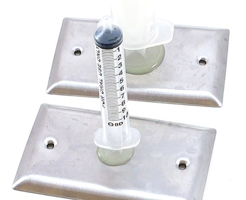 The flat part at the top of a small syringe glued to wall plate. In the background, you see the top of a larger syringe is glued to a second wall plate.