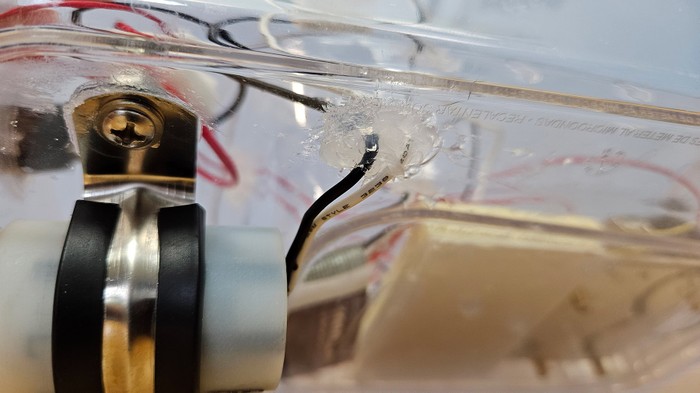 Silicone sealant around two wires passing through the bottom of a plastic container
