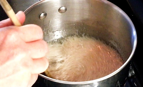 Person stirring a solution that has white to light brown foam bubbling up on it.