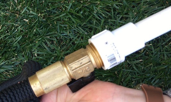A PVC adapter piece connecting a garden hose to a PVC pipe.