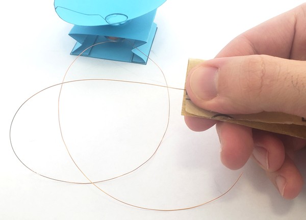 Hand pinching speaker wires between sandpaper.