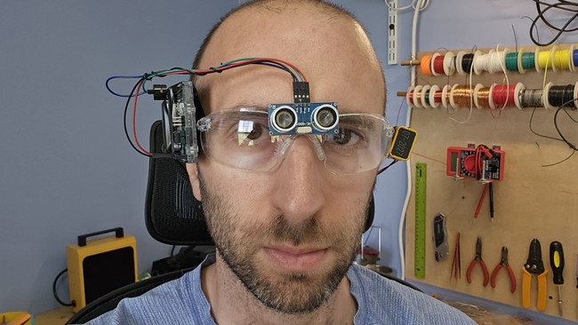 a man wearing safety glasses with an ultrasonic distance sensor mounted on the front