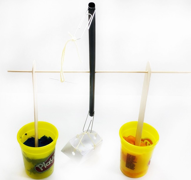 the balance beam with a basket attached on one side and a needle on a string on the other side. The beam tips over as the basket is heavier than the needle.