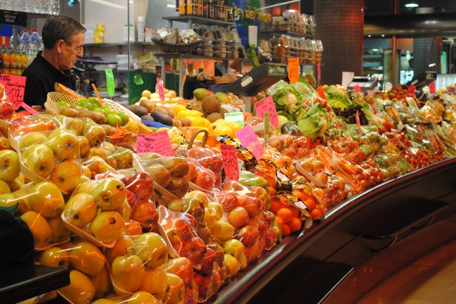 Fruits and vegetables wrapped in plastic displayed in a grocery store.