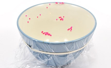 Bowl with colorful sprinkles vibrating on top of tightly-wrapped plastic.