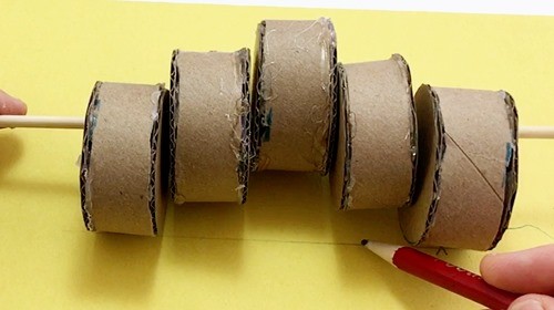 Person making a mark along a line indicating the middle of a cylinder of a set of 5 cylinders attached to a skewer.