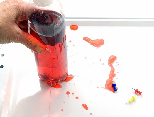 A hand squeezing a bottle with holes. Water flows out of the holes.
