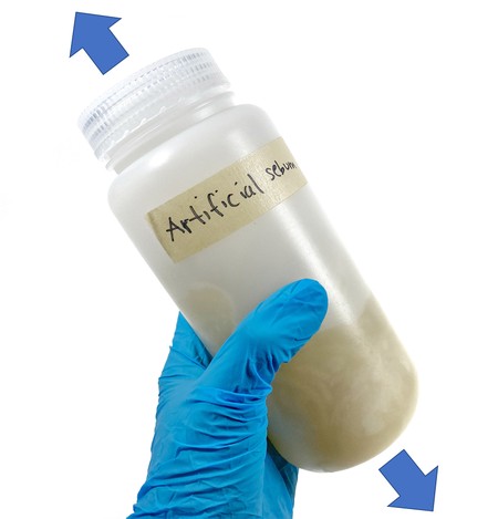 A hand is holding a bottle filled with a yellow liquid. Arrows point up and down from the bottle.
