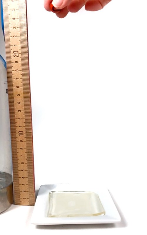 A hand holds a marble above a hydrogel sample, next to a ruler.