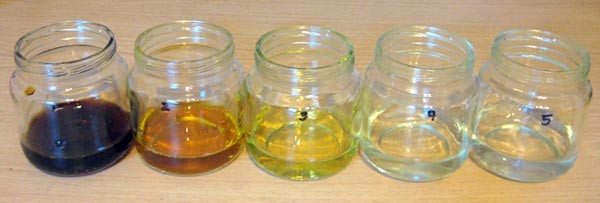 Five glass jars contain solutions of different colors, black, amber, yellow, pale yellow and clear
