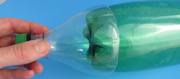 The bottom end of a soda bottle being covered by the top of another soda bottle.