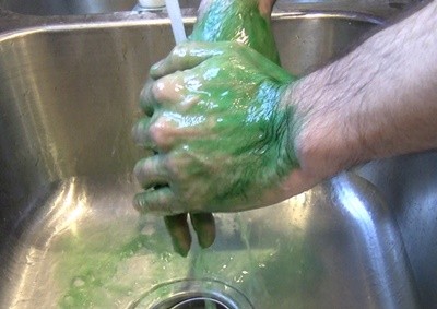 Hands covered in green paint being washed in a sink.
