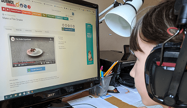 Student wearing headphones and sitting at a computer while watching an online STEM video as part of online learning with her class