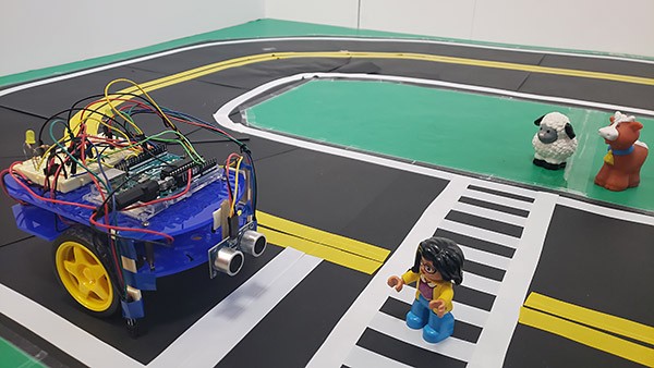 An Arduino robot vehicle, driving on a model road made from construction paper and tape, stops at a crosswalk.
