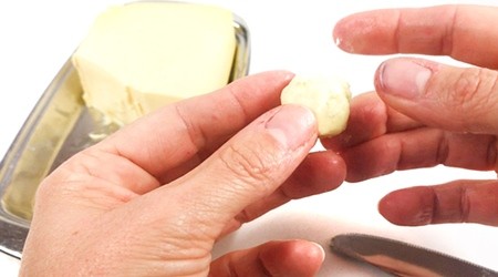 Hands holding an aluminum ball that is covered with butter.