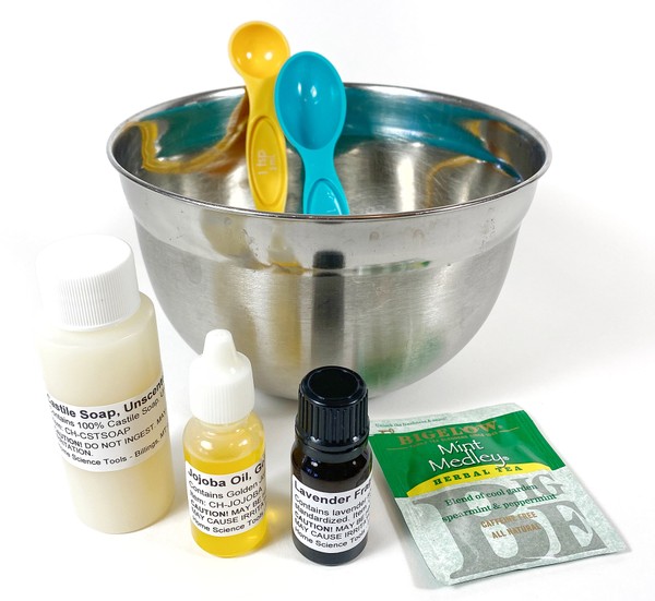 Three small bottles filled with liquid, one herbal tea bag and a bowl with two measuring spoons on a table.