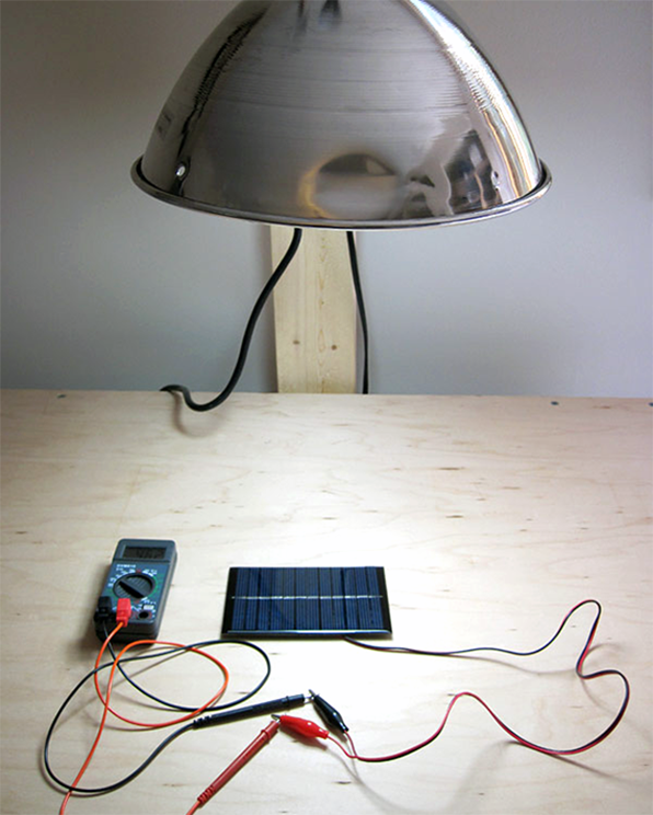 Setup with a solar panel connected to a multimeter and a lamp above