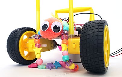 A robot with two wheels facing the camera. The robot is decorated with googly eyes and a necklace.