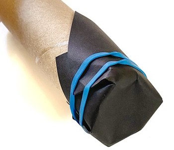 A cardboard tube with black cardstock paper wrapped around one of its openings. A rubber band holds the cardstock paper in place.