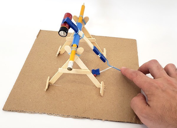 A hand holding the trebuchet sling down, ready to launch. 