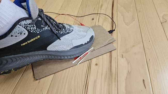 A foot pressing down on a cardboard foot pedal