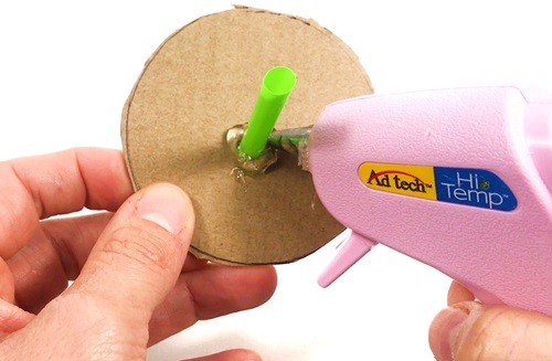 Person putting hot glue around a straw that is inserted through a hole in a cardboard circle.