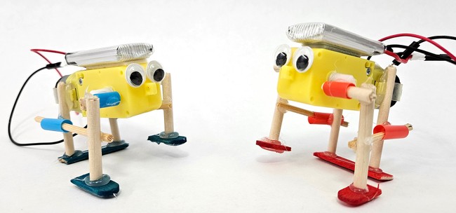 Two walking robots made from DC motors, wooden dowels, straws, and popsicle sticks