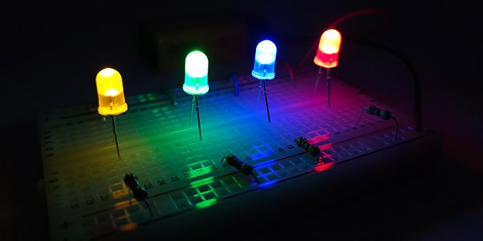 Red, blue, yellow, and green LEDs on a white breadboard, illuminating it in the dark